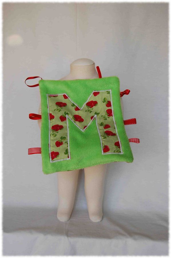 Doudou plat rectangulaire en polaire vert, lettre M en coton vichy vert impression fraises et rubans rouges