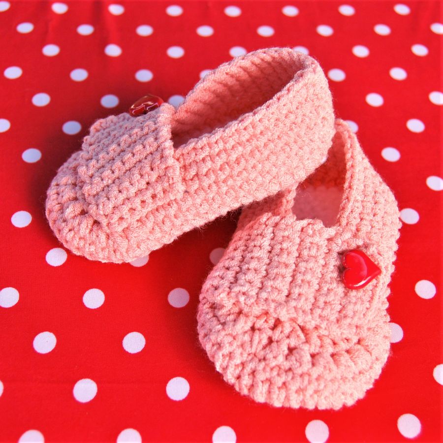 Paire de chaussons roses bébé crochetées main avec un bouton en forme de coeur rouge sur la languette 