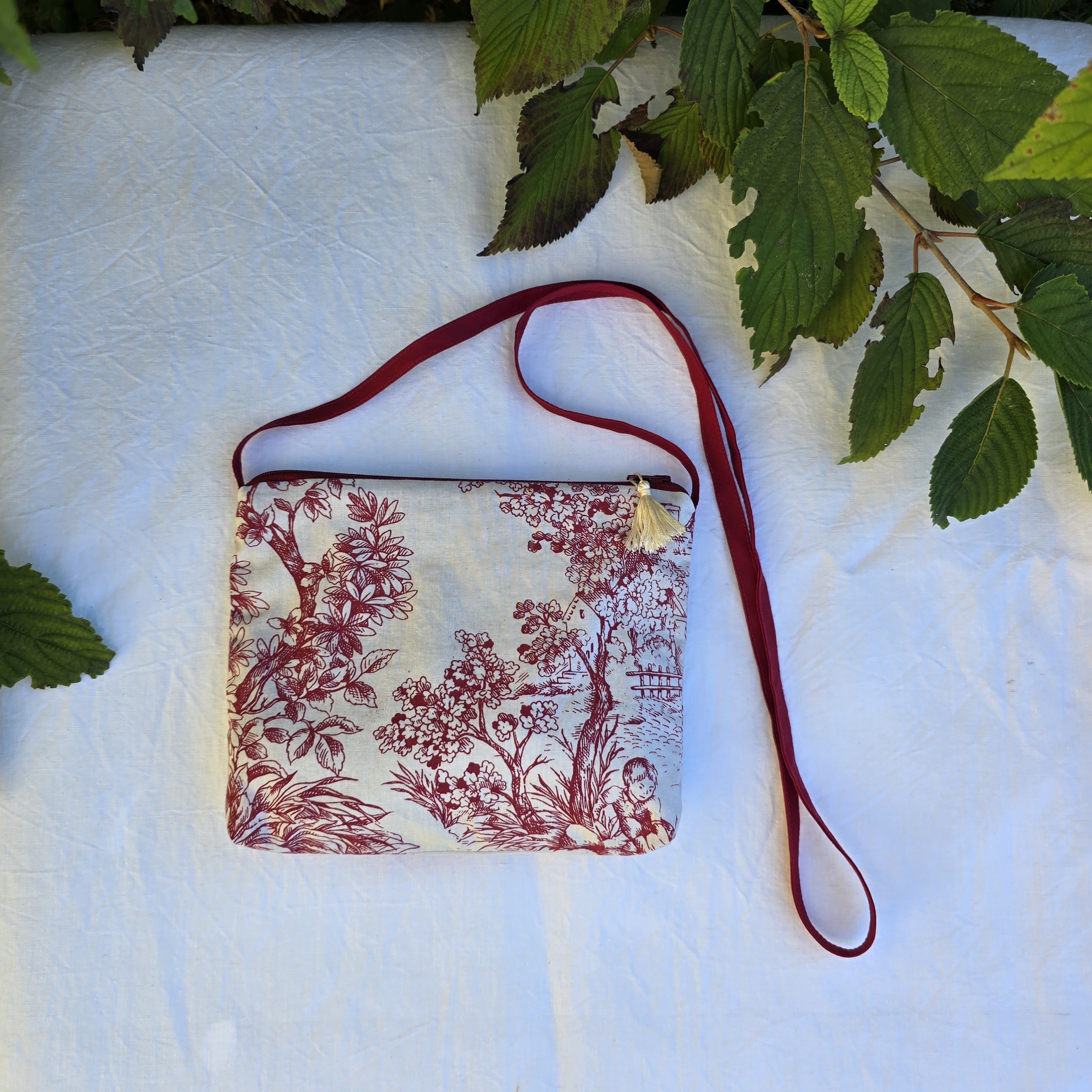 Pochette avec bandoulière en tissu toile de Jouy bordeaux et écru agrémentée d'un pompon