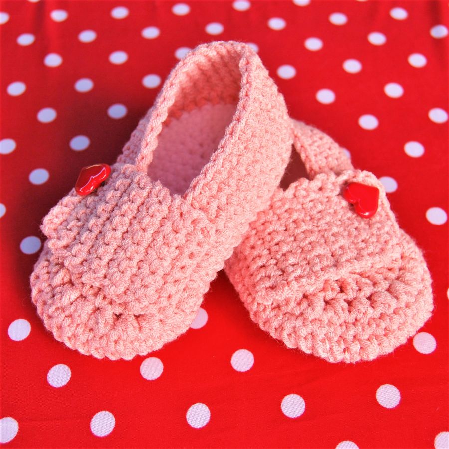 Paire de chaussons roses poupée crochetées main avec un bouton en forme de coeur rouge sur la languette 