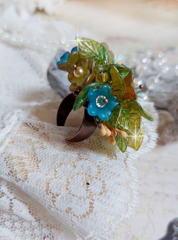 Bague Cézanne montée avec des petites fleurs lucites peintes à la main à laquelle s’ajoute des feuilles, cristaux, perles, étamines, grosses rocailles, perles nacrées et métal sur une bague en Laiton