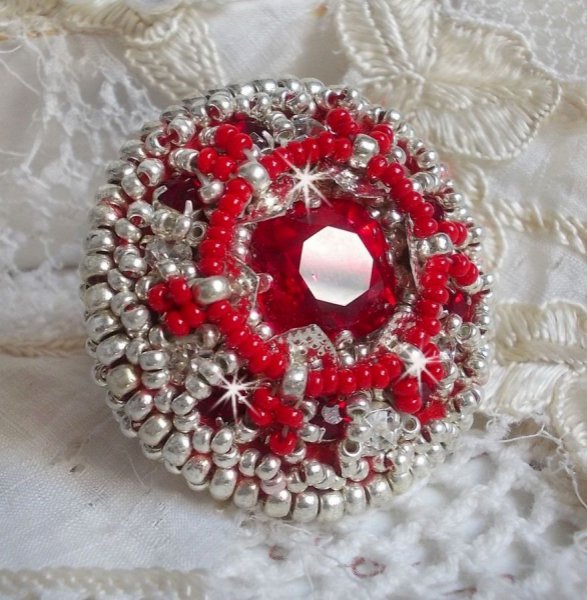 Bague Drigon Red brod&eacute;e avec un cabochon carr&eacute; Rouge sur une estampe Argent&eacute;e. Orn&eacute;e de chatons en Cristal puis model&eacute;e avec des rocailles et perles. Le tout est mont&eacute; sur une bague r&eacute;glable argent&eacute;e 