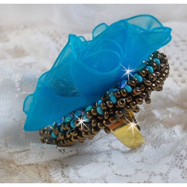Bague Ilycia Charming brod&eacute;e avec un cabochon facett&eacute; Bleu Turquoise, fleur en Cristal, chatons, rocailles Gold et Bronze. Le tout est mont&eacute; sur un support de bague couleur Or en laiton