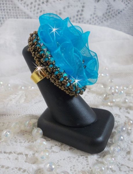 Bague Ilycia Charming brod&eacute;e avec un cabochon facett&eacute; Bleu Turquoise, fleur en Cristal, chatons, rocailles Gold et Bronze. Le tout est mont&eacute; sur un support de bague couleur Or en laiton
