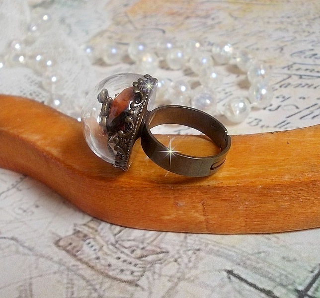 Bague Majest&eacute; Steampunk aux rouages m&eacute;caniques &agrave; laquelle s&rsquo;ajoute une cl&eacute; et un strass de couleur Siam et un strass en verre Dor&eacute;. Le tout est mis sous un globe en verre sur une bague r&eacute;glable laiton