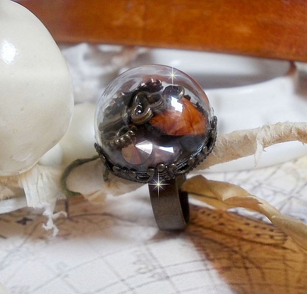 Bague Majest&eacute; Steampunk aux rouages m&eacute;caniques &agrave; laquelle s&rsquo;ajoute une cl&eacute; et un strass de couleur Siam et un strass en verre Dor&eacute;. Le tout est mis sous un globe en verre sur une bague r&eacute;glable laiton