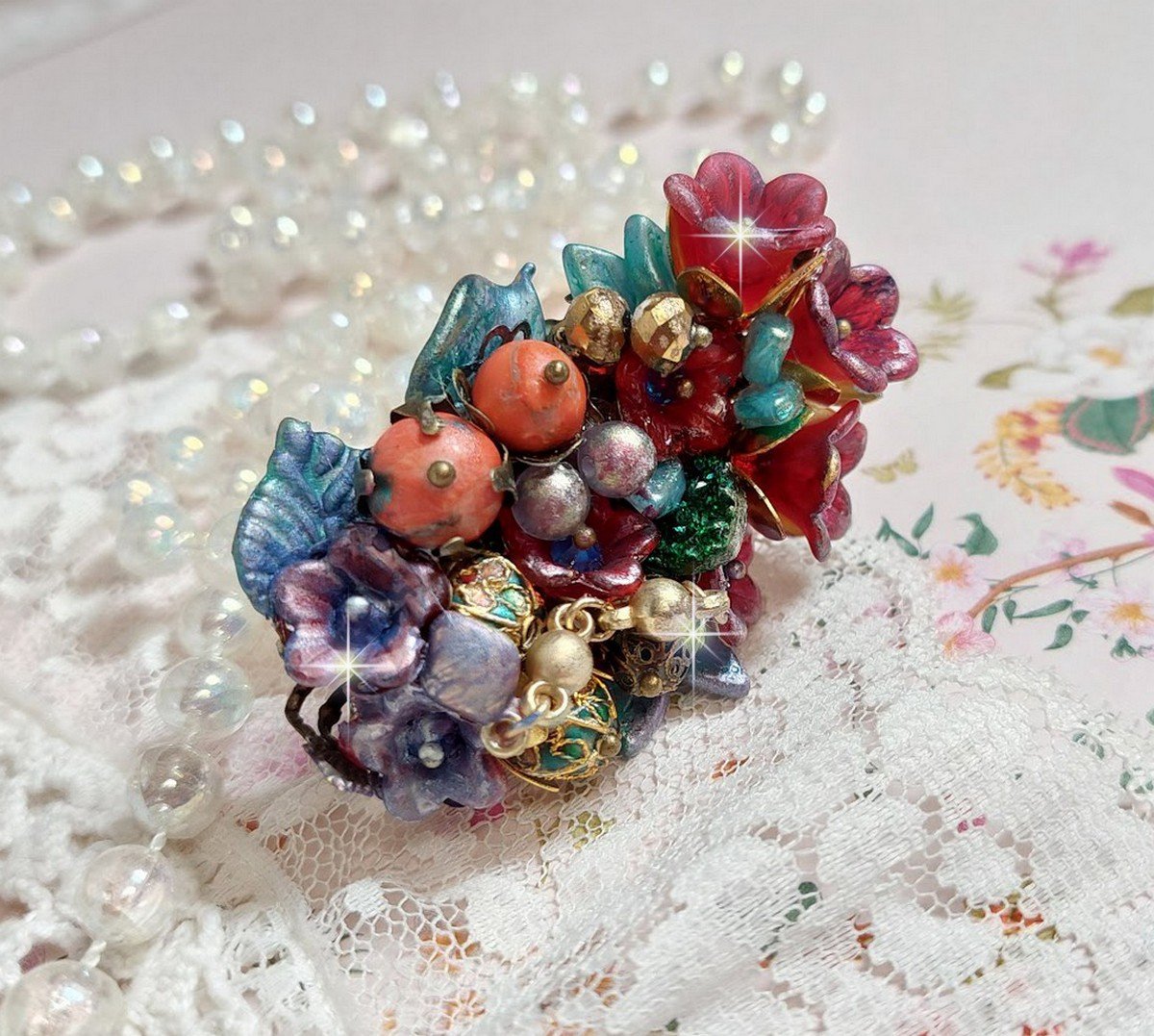 Bague Onia pour une composition florale créée avec des cristaux, fleurs : perles, clochettes, pensées, gouttes Druzy,  pierre de gemme : le Corail, perles cloisonnées et bague ovale en Laiton