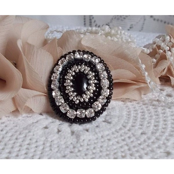 Bague Stone Noire avec un cabochon en Onyx orn&eacute; de chatons en Cristal &agrave; laquelle s&rsquo;ajoute des rocailles Argent&eacute;es qui compl&egrave;tent le Noir sur bague Nickel en Laiton et une feutrine. Un style R&eacute;tro