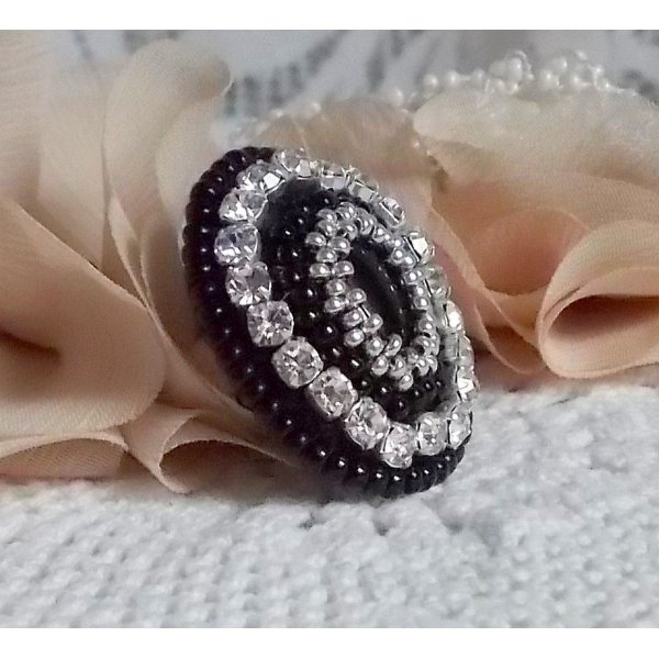 Bague Stone Noire avec un cabochon en Onyx orn&eacute; de chatons en Cristal &agrave; laquelle s&rsquo;ajoute des rocailles Argent&eacute;es qui compl&egrave;tent le Noir sur bague Nickel en Laiton et une feutrine. Un style R&eacute;tro