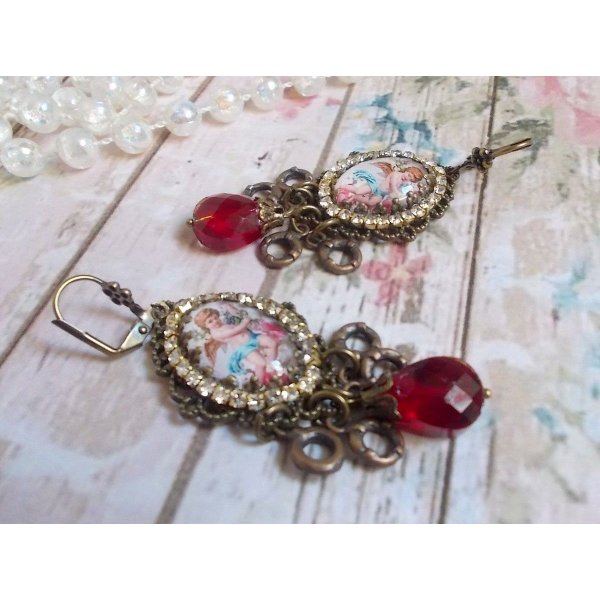 BO Petit Ange avec des cabochons d&rsquo;anges orn&eacute;s d&rsquo;une cha&icirc;ne strass Cristal, breloques, gouttes facett&eacute;es en verre de couleur Siam. Mont&eacute;s sur des pendentifs et des dormeuses en Laiton