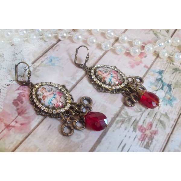 BO Petit Ange avec des cabochons d&rsquo;anges orn&eacute;s d&rsquo;une cha&icirc;ne strass Cristal, breloques, gouttes facett&eacute;es en verre de couleur Siam. Mont&eacute;s sur des pendentifs et des dormeuses en Laiton