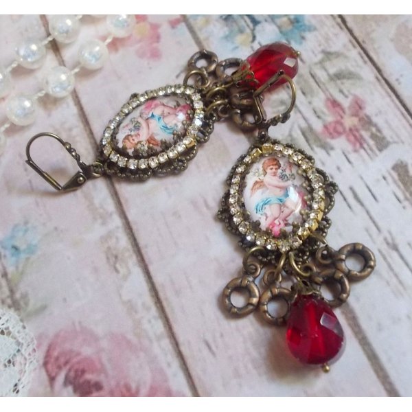 BO Petit Ange avec des cabochons d&rsquo;anges orn&eacute;s d&rsquo;une cha&icirc;ne strass Cristal, breloques, gouttes facett&eacute;es en verre de couleur Siam. Mont&eacute;s sur des pendentifs et des dormeuses en Laiton