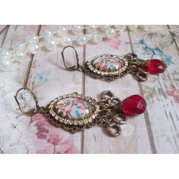 BO Petit Ange avec des cabochons d&rsquo;anges orn&eacute;s d&rsquo;une cha&icirc;ne strass Cristal, breloques, gouttes facett&eacute;es en verre de couleur Siam. Mont&eacute;s sur des pendentifs et des dormeuses en Laiton