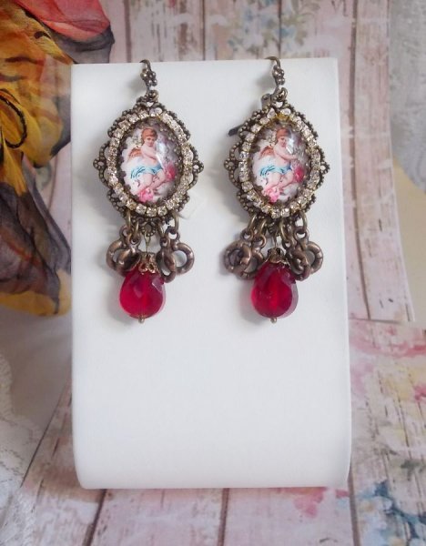 BO Petit Ange avec des cabochons d&rsquo;anges orn&eacute;s d&rsquo;une cha&icirc;ne strass Cristal, breloques, gouttes facett&eacute;es en verre de couleur Siam. Mont&eacute;s sur des pendentifs et des dormeuses en Laiton