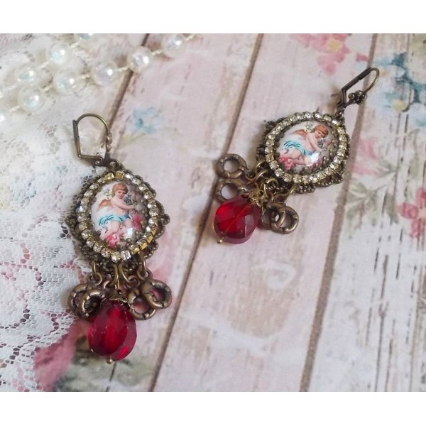 BO Petit Ange avec des cabochons d&rsquo;anges orn&eacute;s d&rsquo;une cha&icirc;ne strass Cristal, breloques, gouttes facett&eacute;es en verre de couleur Siam. Mont&eacute;s sur des pendentifs et des dormeuses en Laiton