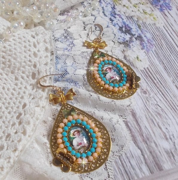 BO Mademoiselle Noellia avec des cabochons ovales repr&eacute;sentant une femme avec un chapeau et un n&oelig;ud blanc &agrave; laquelle s&rsquo;ajoute des cristaux, cha&icirc;nes strass P&ecirc;che et Turquoise sur crochets en plaqu&eacute; Or