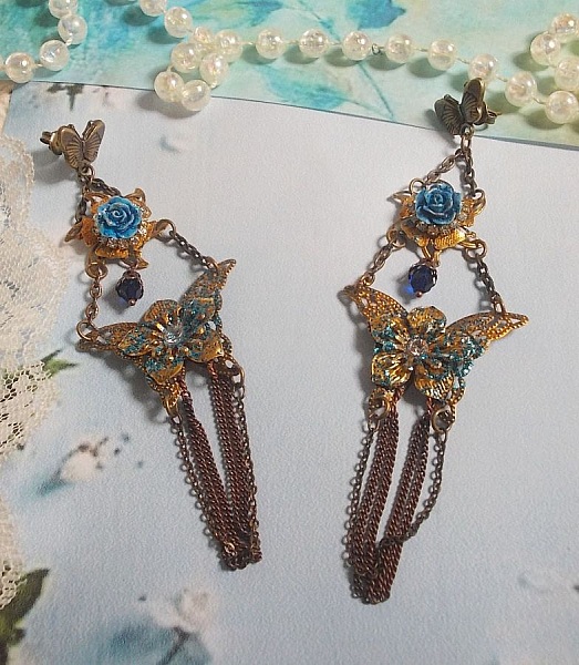 BO Papillons Iris&eacute;s mont&eacute;s sur estampes paillet&eacute;es de Bleu et Bronze, cabochons en forme de rose &agrave; laquelle s&rsquo;ajoute : coupelles fleurs, cha&icirc;ne strass, Zirconiums Cristal et gouttes Cobalt