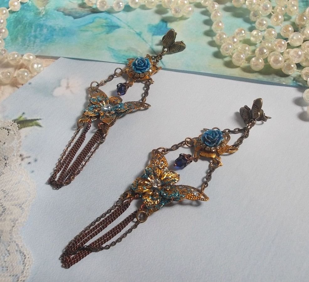 BO Papillons Irisés montés sur estampes pailletées de Bleu et Bronze, cabochons en forme de rose à laquelle s’ajoute : coupelles fleurs, chaîne strass, Zirconiums Cristal et gouttes Cobalt