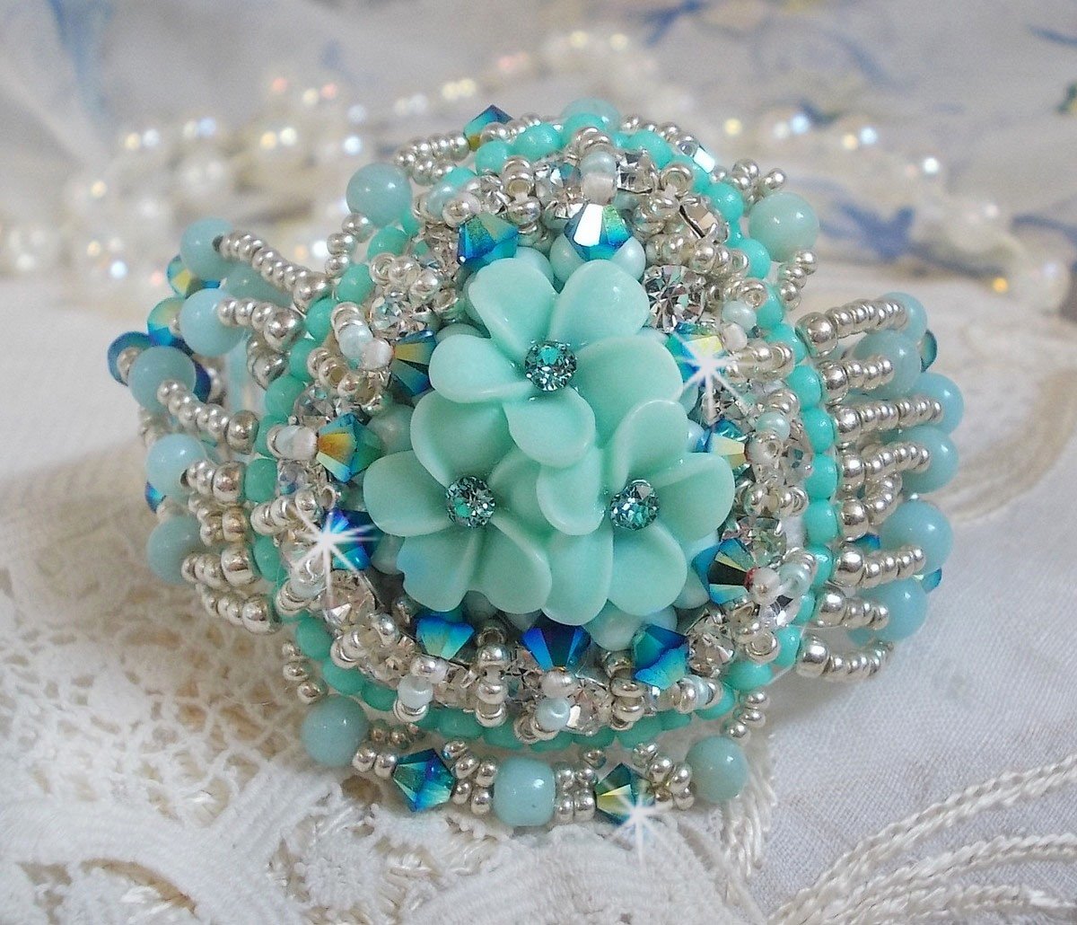 Bracelet Blue Flowers Haute-Couture brodé avec des Cristaux de Swarovski, un cabochon en résine, des perles rondes en satin, des rocailles avec une chaînette et un fermoir en Argent 925/1000