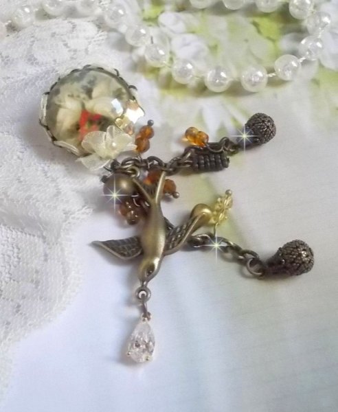 Broche Colombes aux plumages blancs avec des breloques filigran&eacute;es gouttes et lisses, perles rondes et n&oelig;ud en cristal, ruban organza cr&egrave;me, pendentif plaqu&eacute; or avec un zircon sur une broche en m&eacute;tal