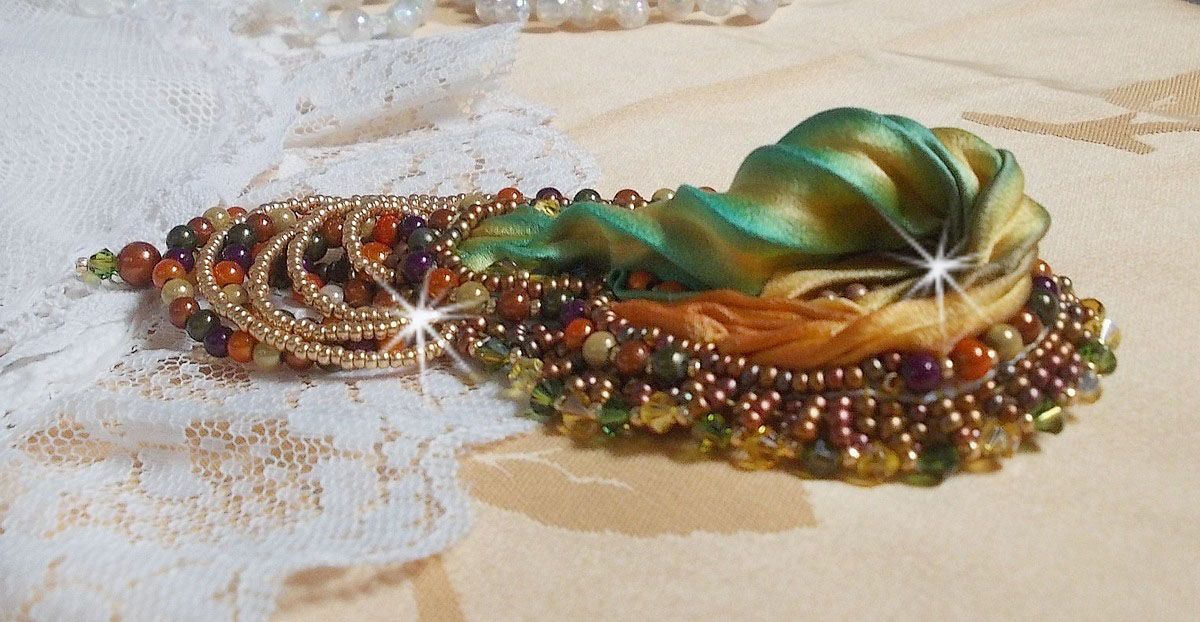 Broche Lune Vénitienne brodée avec un ruban de soie orange, vert et jaune, cristaux, : toupies et chatons. S’ajoute à l’ensemble des perles magiques et rocailles sur une broche Doré 