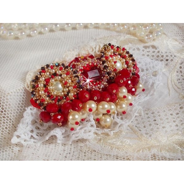 Broche Rubis brod&eacute;e avec trois cabochons Ivoire et Rouge &agrave; laquelle s&rsquo;ajoute des toupies aux couleurs Cristal, Burgundy et Garnet, des perles nacr&eacute;es et opaque. Mont&eacute; sur une dentelle et une broche