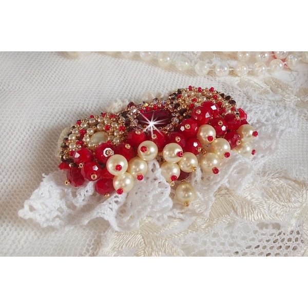 Broche Rubis brod&eacute;e avec trois cabochons Ivoire et Rouge &agrave; laquelle s&rsquo;ajoute des toupies aux couleurs Cristal, Burgundy et Garnet, des perles nacr&eacute;es et opaque. Mont&eacute; sur une dentelle et une broche