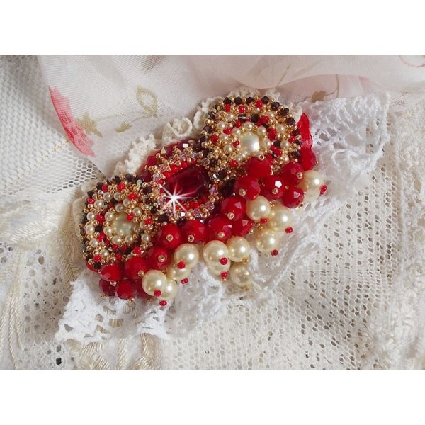 Broche Rubis brod&eacute;e avec trois cabochons Ivoire et Rouge &agrave; laquelle s&rsquo;ajoute des toupies aux couleurs Cristal, Burgundy et Garnet, des perles nacr&eacute;es et opaque. Mont&eacute; sur une dentelle et une broche
