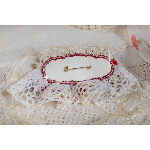Broche Rubis brod&eacute;e avec trois cabochons Ivoire et Rouge &agrave; laquelle s&rsquo;ajoute des toupies aux couleurs Cristal, Burgundy et Garnet, des perles nacr&eacute;es et opaque. Mont&eacute; sur une dentelle et une broche