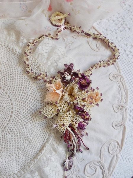 Collier Les Floralies sur une base Netting, j&rsquo;ai r&eacute;alis&eacute; &agrave; l&rsquo;aiguille un bouquet de fleurs et feuilles en rocailles &agrave; laquelle s&rsquo;ajoute des Sugilites. Aux couleurs Ivoire, Am&eacute;thyste, Rose et Purple