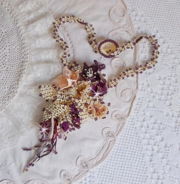 Collier Les Floralies sur une base Netting, j&rsquo;ai r&eacute;alis&eacute; &agrave; l&rsquo;aiguille un bouquet de fleurs et feuilles en rocailles &agrave; laquelle s&rsquo;ajoute des Sugilites. Aux couleurs Ivoire, Am&eacute;thyste, Rose et Purple