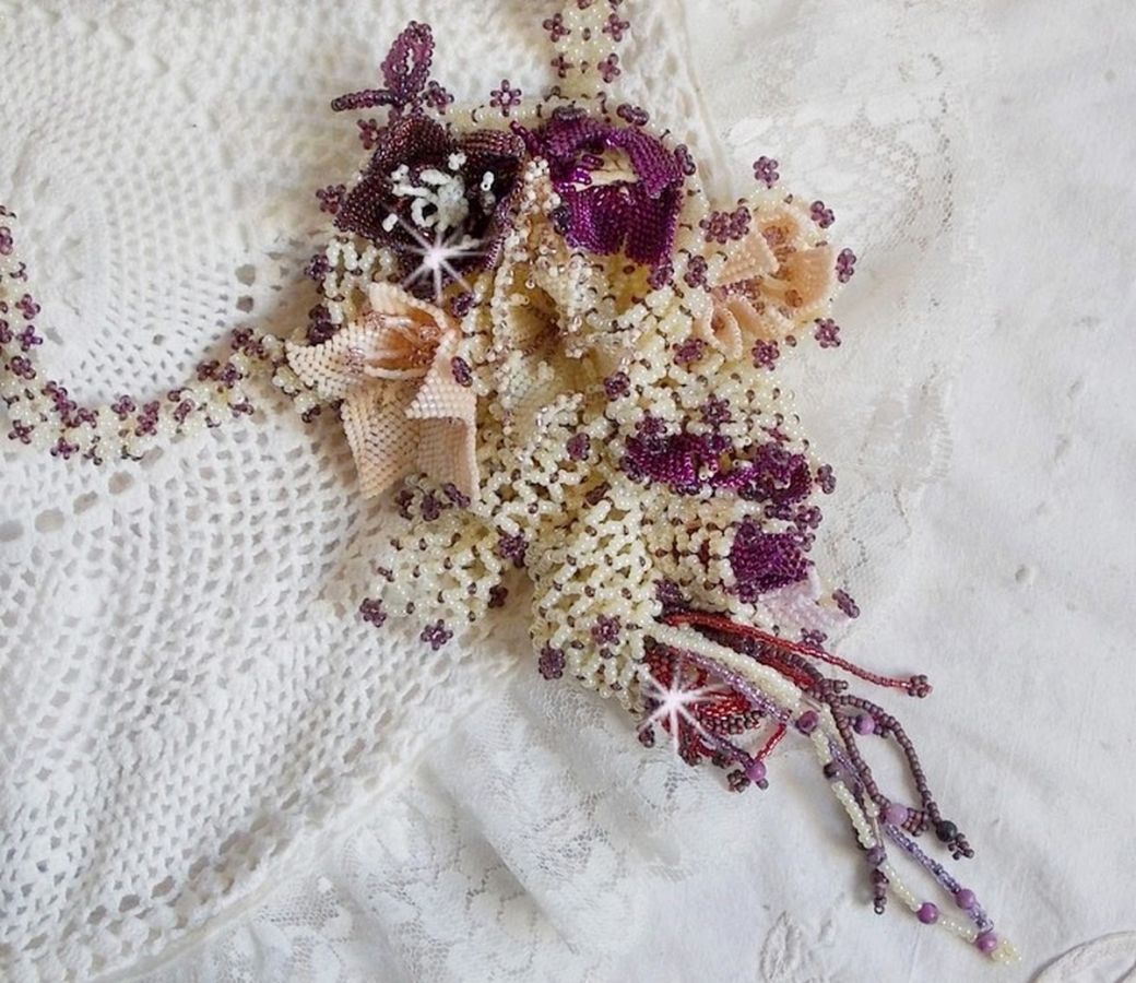 Collier Les Floralies sur une base Netting, j’ai réalisé à l’aiguille un bouquet de fleurs et feuilles en rocailles à laquelle s’ajoute des Sugilites. Aux couleurs Ivoire, Améthyste, Rose et Purple