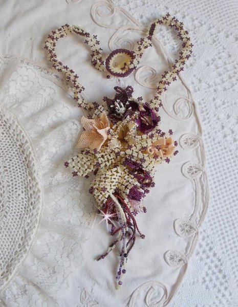 Collier Les Floralies sur une base Netting, j&rsquo;ai r&eacute;alis&eacute; &agrave; l&rsquo;aiguille un bouquet de fleurs et feuilles en rocailles &agrave; laquelle s&rsquo;ajoute des Sugilites. Aux couleurs Ivoire, Am&eacute;thyste, Rose et Purple
