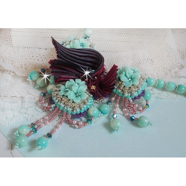 Collier Blue Flowers brod&eacute; avec un ruban de soie framboise/truffe &agrave; laquelle s&rsquo;ajoute : cabochons, perles nacr&eacute;es Rosaline et Ivoire, toupies Jet, anneaux ovales, perles marbr&eacute;es Bleu Ciel et Blanc