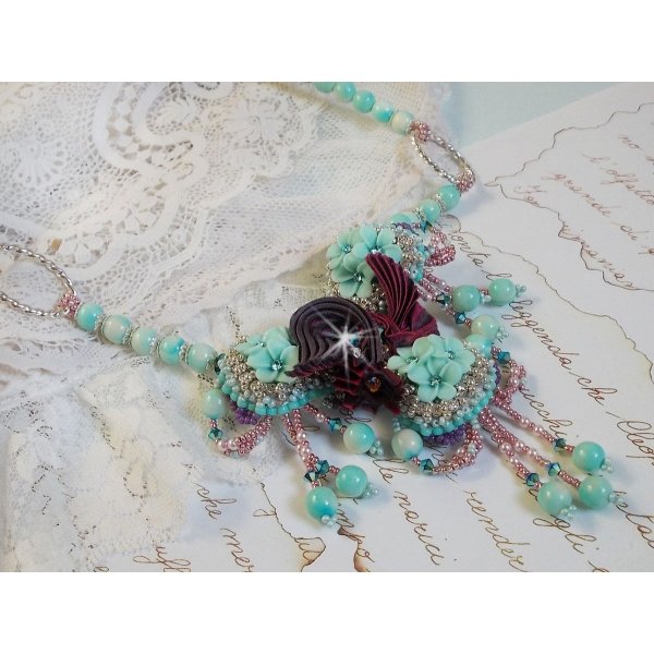 Collier Blue Flowers brod&eacute; avec un ruban de soie framboise/truffe &agrave; laquelle s&rsquo;ajoute : cabochons, perles nacr&eacute;es Rosaline et Ivoire, toupies Jet, anneaux ovales, perles marbr&eacute;es Bleu Ciel et Blanc