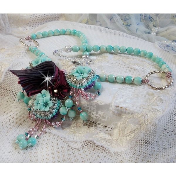 Collier Blue Flowers brod&eacute; avec un ruban de soie framboise/truffe &agrave; laquelle s&rsquo;ajoute : cabochons, perles nacr&eacute;es Rosaline et Ivoire, toupies Jet, anneaux ovales, perles marbr&eacute;es Bleu Ciel et Blanc