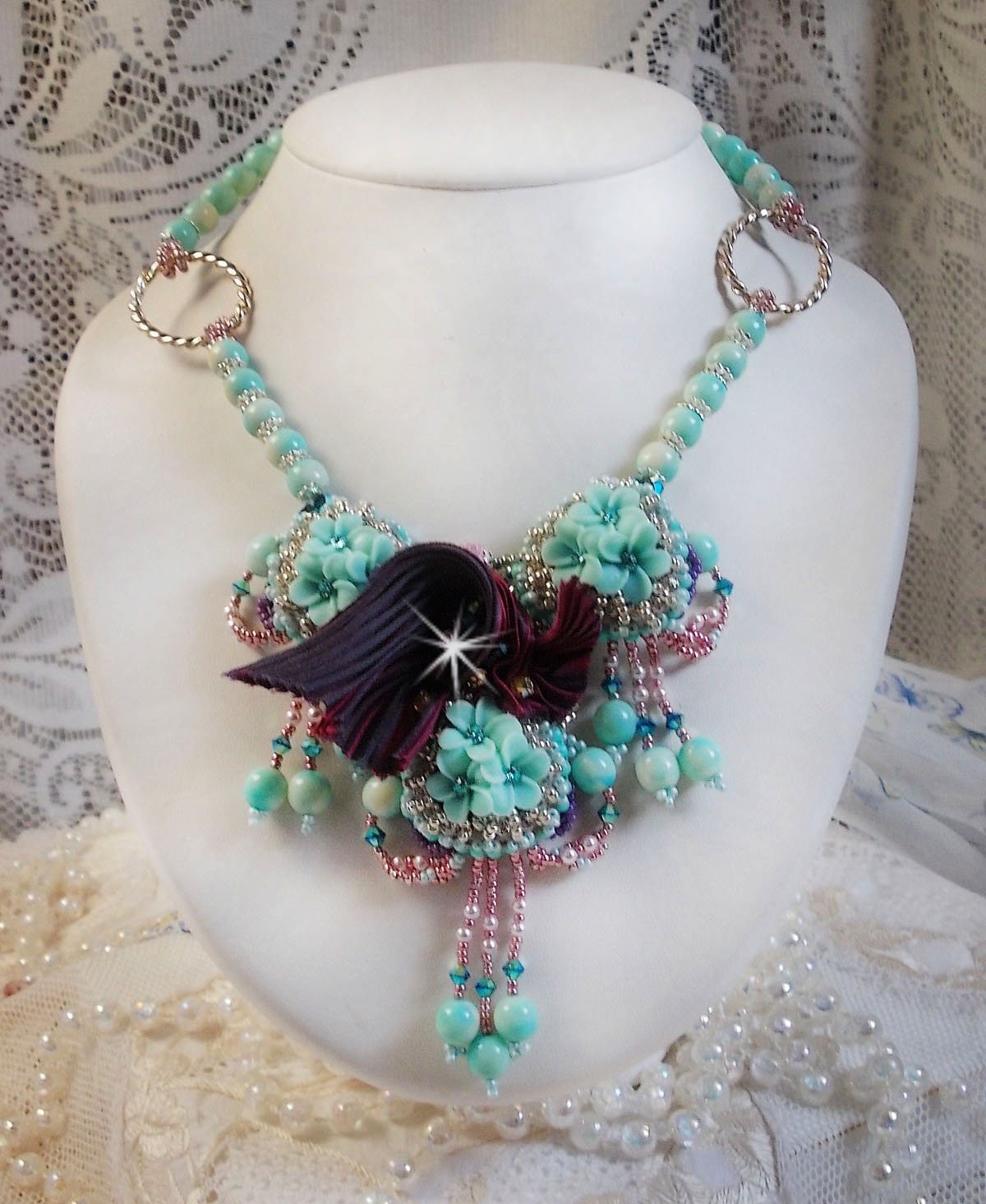 Collier Blue Flowers brod&eacute; avec un ruban de soie framboise/truffe &agrave; laquelle s&rsquo;ajoute : cabochons, perles nacr&eacute;es Rosaline et Ivoire, toupies Jet, anneaux ovales, perles marbr&eacute;es Bleu Ciel et Blanc