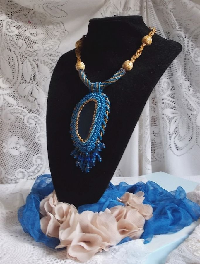 Pendentif Corsica avec un cabochon : une Agate Bleue brodée avec des perles nacrées Bleu Lapis en cristal à laquelle s’ajoute des rocailles saphir et travertin entrelacées pour former une dentelle