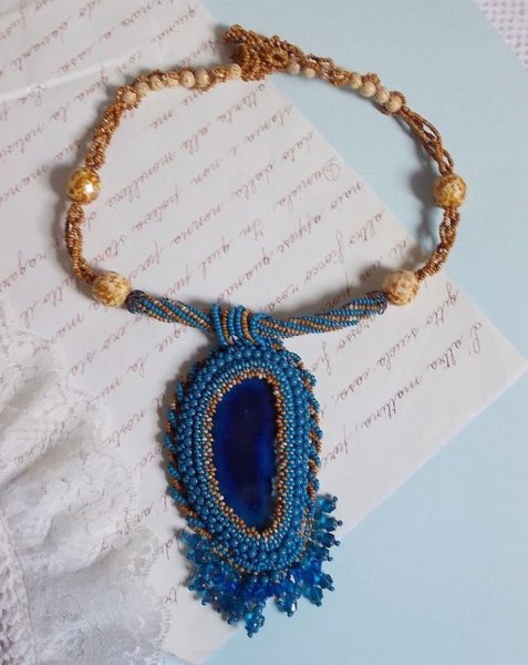 Pendentif Corsica avec un cabochon : une Agate Bleue brod&eacute;e avec des perles nacr&eacute;es Bleu Lapis en cristal &agrave; laquelle s&rsquo;ajoute des rocailles saphir et travertin entrelac&eacute;es pour former une dentelle