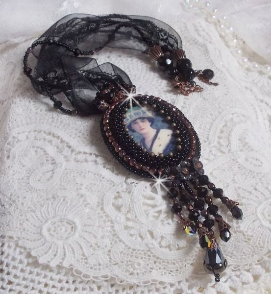 Pendentif Midnight Daisy avec un cabochon en bois repr&eacute;sentant une femme en chapeau Bleu, brod&eacute; avec des fleurs lucites, coupelles et facettes. Le tout est fini avec une dentelle Noire et un ruban