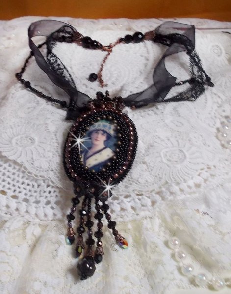 Pendentif Midnight Daisy avec un cabochon en bois repr&eacute;sentant une femme en chapeau Bleu, brod&eacute; avec des fleurs lucites, coupelles et facettes. Le tout est fini avec une dentelle Noire et un ruban