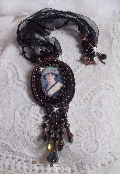 Pendentif Midnight Daisy avec un cabochon en bois repr&eacute;sentant une femme en chapeau Bleu, brod&eacute; avec des fleurs lucites, coupelles et facettes. Le tout est fini avec une dentelle Noire et un ruban