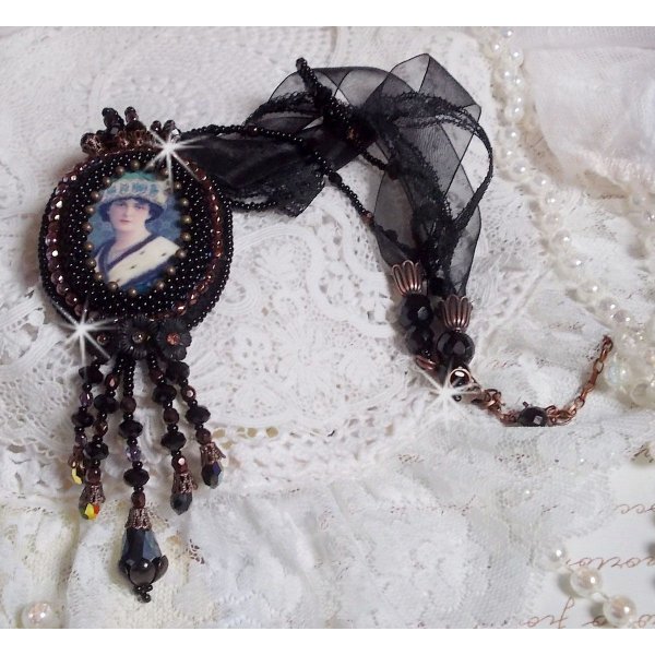 Pendentif Midnight Daisy avec un cabochon en bois repr&eacute;sentant une femme en chapeau Bleu, brod&eacute; avec des fleurs lucites, coupelles et facettes. Le tout est fini avec une dentelle Noire et un ruban