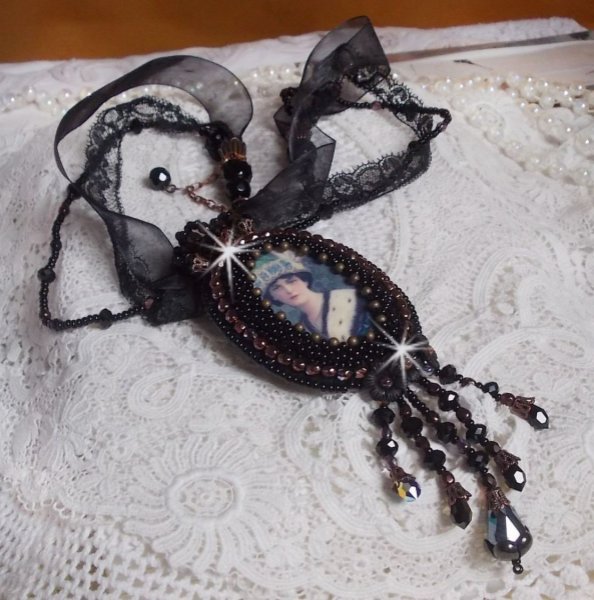 Pendentif Midnight Daisy avec un cabochon en bois repr&eacute;sentant une femme en chapeau Bleu, brod&eacute; avec des fleurs lucites, coupelles et facettes. Le tout est fini avec une dentelle Noire et un ruban