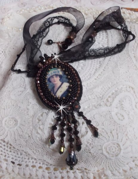 Pendentif Midnight Daisy avec un cabochon en bois repr&eacute;sentant une femme en chapeau Bleu, brod&eacute; avec des fleurs lucites, coupelles et facettes. Le tout est fini avec une dentelle Noire et un ruban