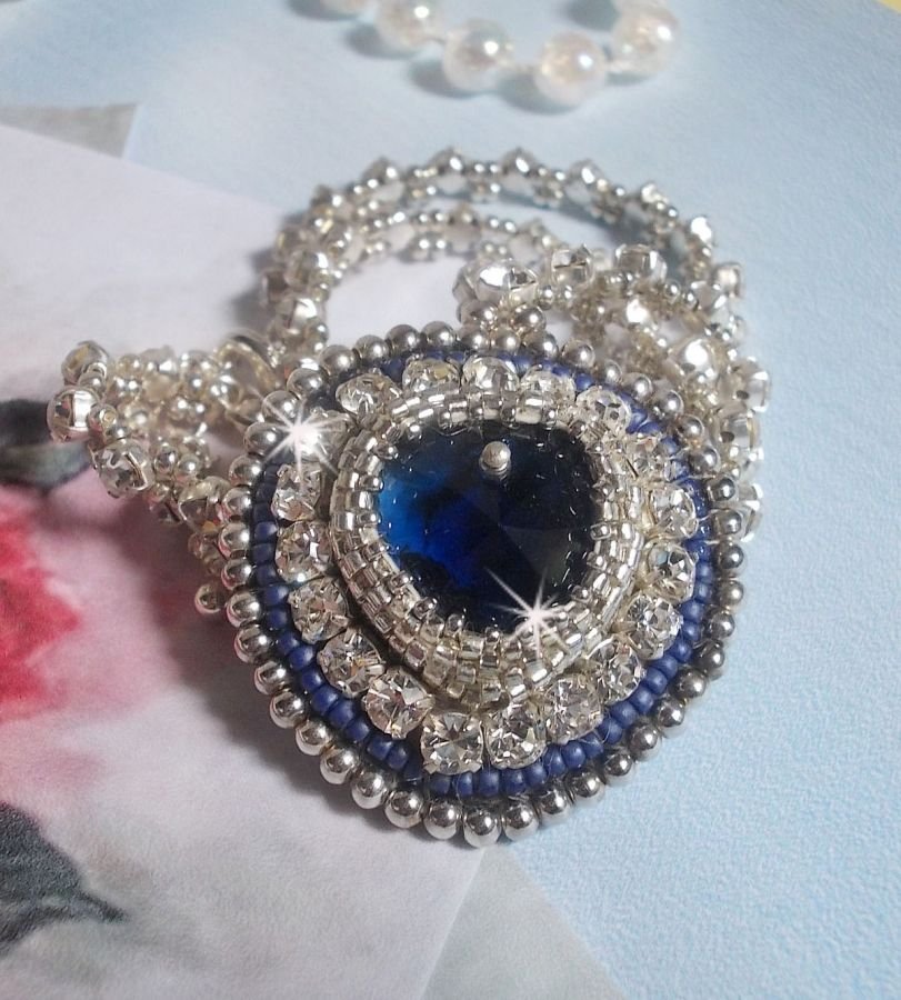 Collier Saphir Bleu brodé à l'aiguille avec un cœur en cristal de Swarovski, rocailles argentées Miyuki, strass, un fermoir et une chaînette d'extension en argent 925/1000. Un voyage si lointain.