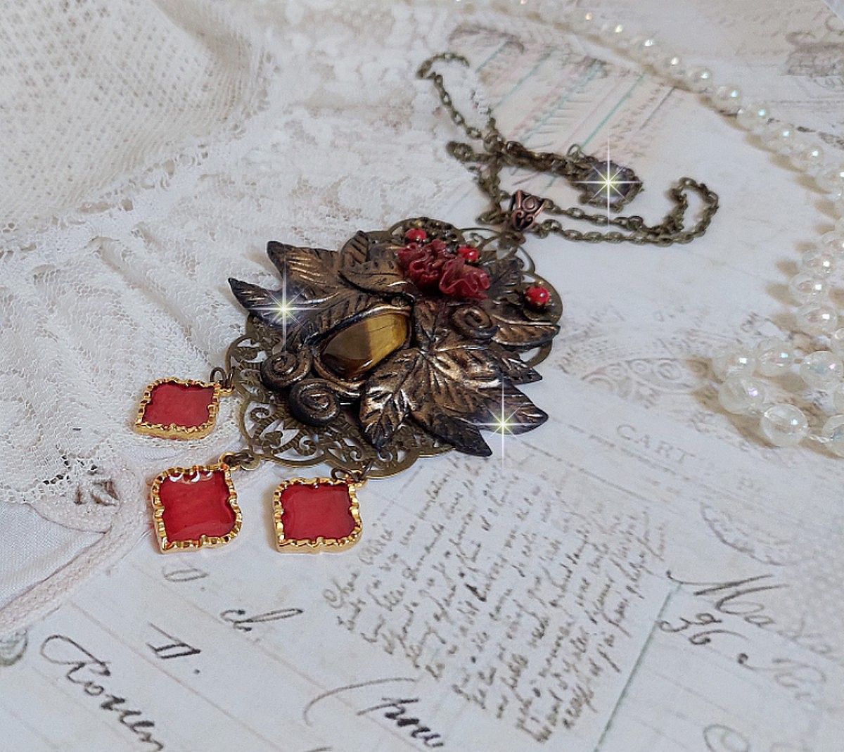 Pendentif Mélodie avec un cabochon Œil de tigre orné de perles en Jade Rouge veiné de Noir sur fleurs 5 pétales et estampes montés sur une chaîne bronze. Les pendants sont en résine époxy Rouge