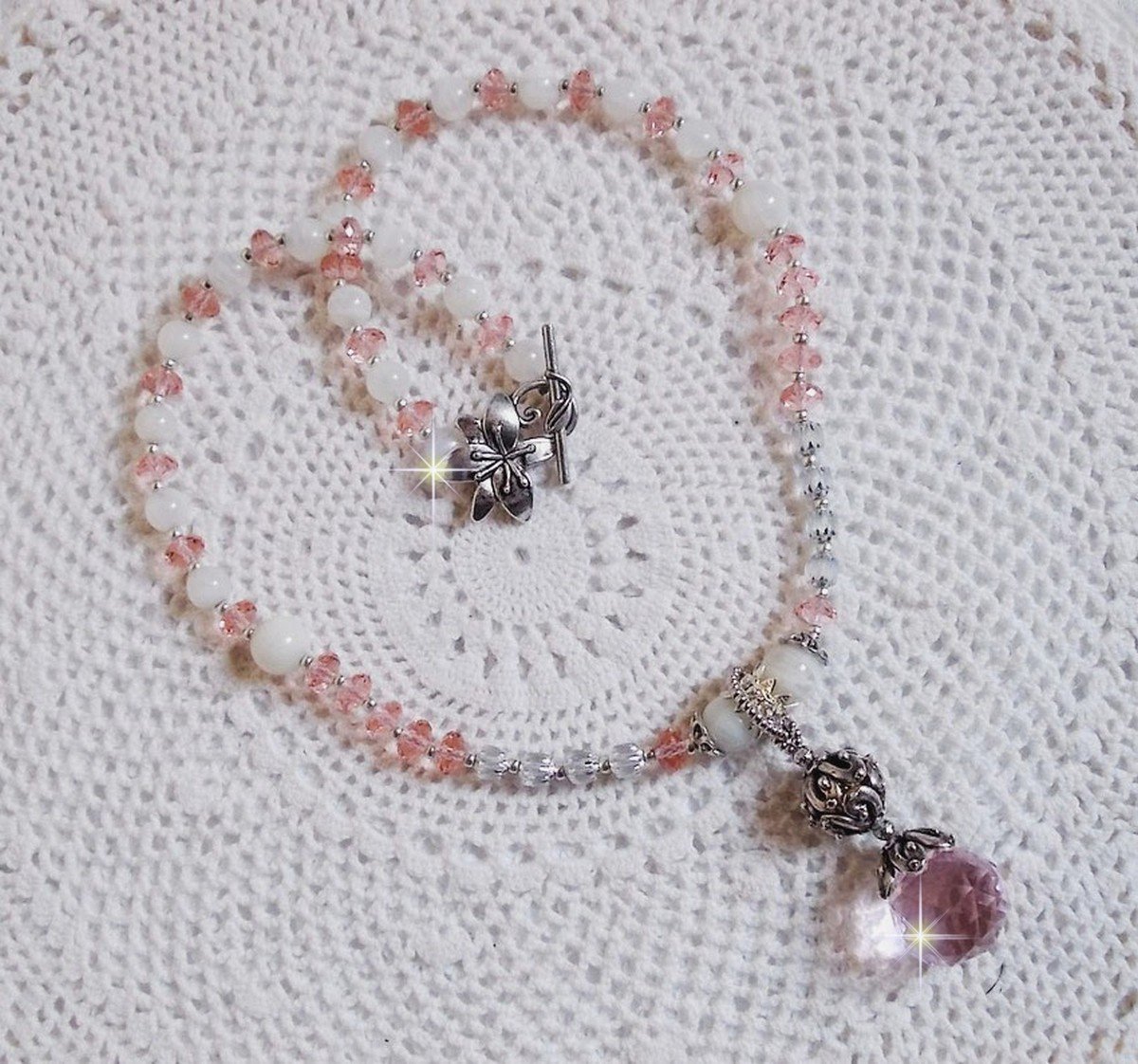 Pendentif Rose Irisé monté avec des perles rondes aplaties en cristal, des perles de gemme : la pierre de lune, des coupelles dômes, une perle d’espacement strassée, perles lisses et filigranées